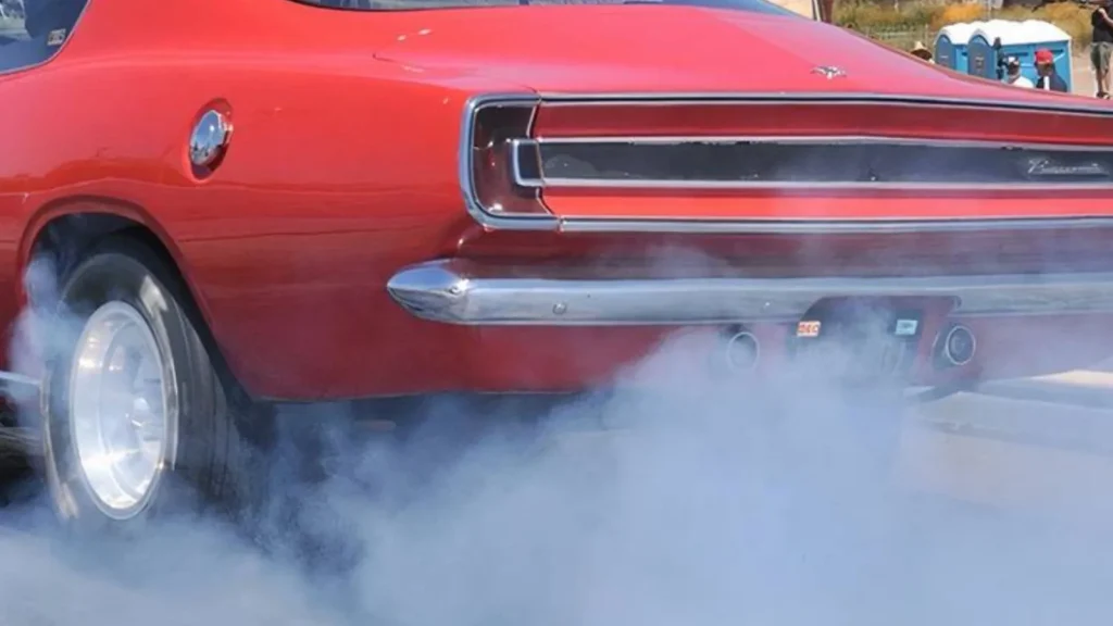 Plymouth Barracuda rouge de la fin des années 60 faisant un burn-out, roue arrière dans la fumée