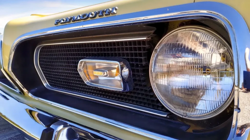 Détail de la calandre chromée et du phare rond d'une Plymouth Barracuda 1969 de couleur or